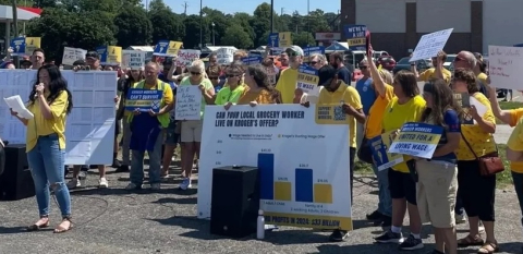 A group of 50 in yellow union shirts rallies in a grocery store parking lot.