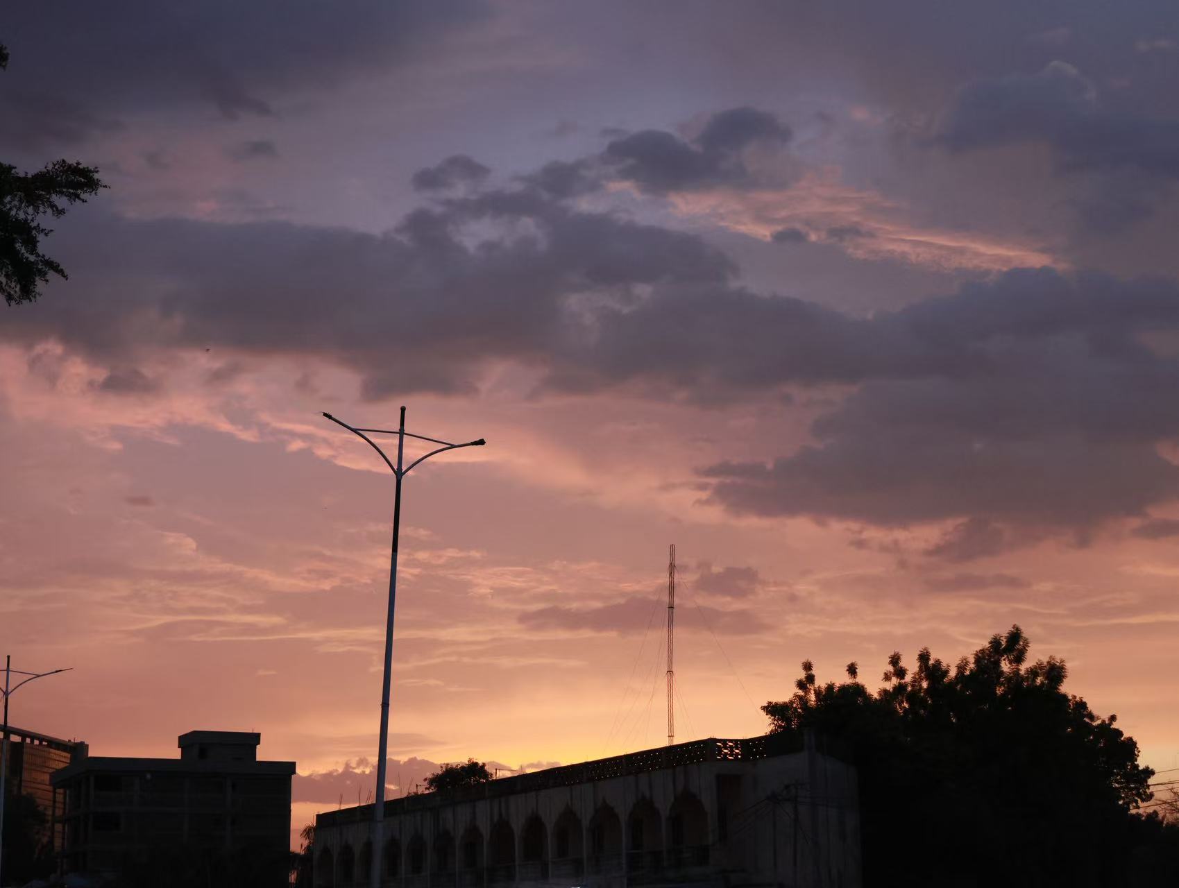 Purple and orange evening clouds hang over a neighborhood in N'Djamena as streetlights and rooftops fade into dusk.