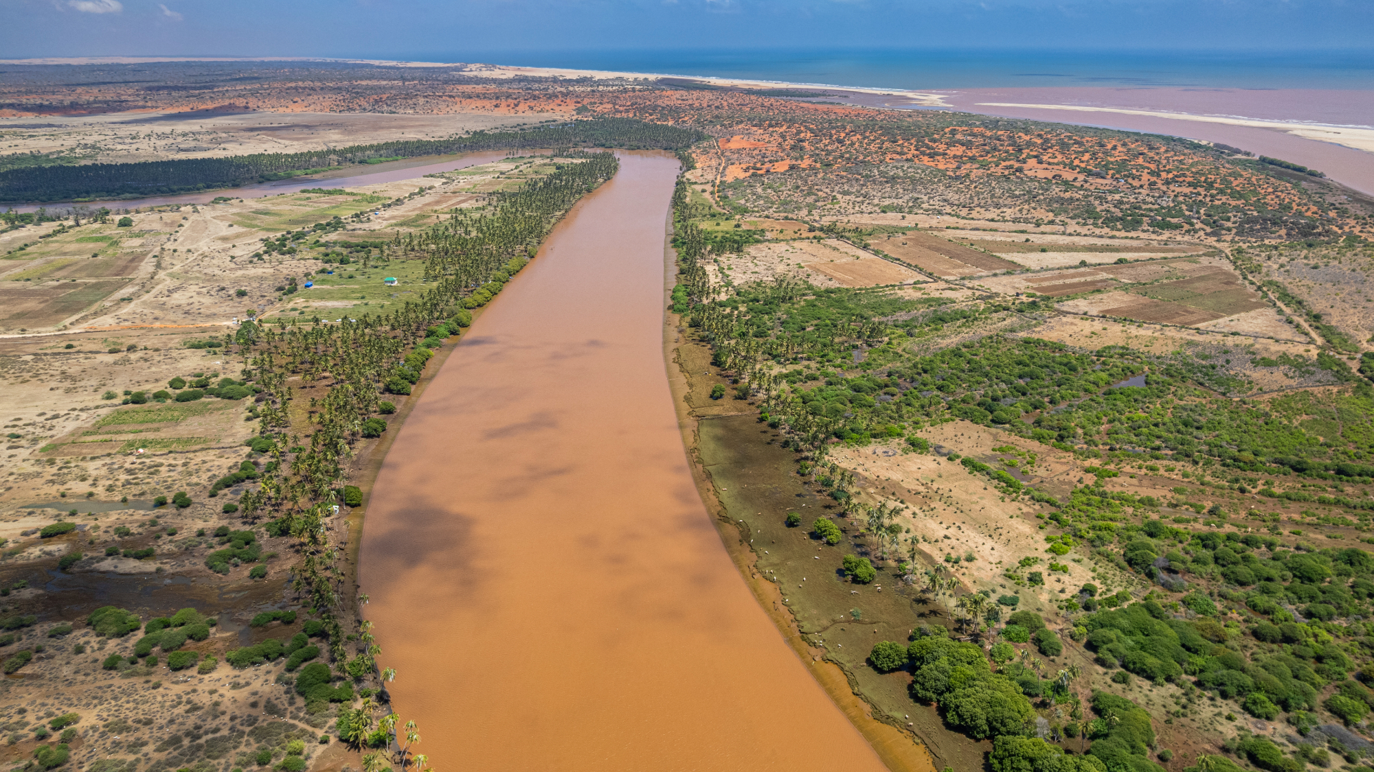 Aerial view of Juba river winding through landscape with vegetation and coastal area in the distance near Kismayo, Somalia