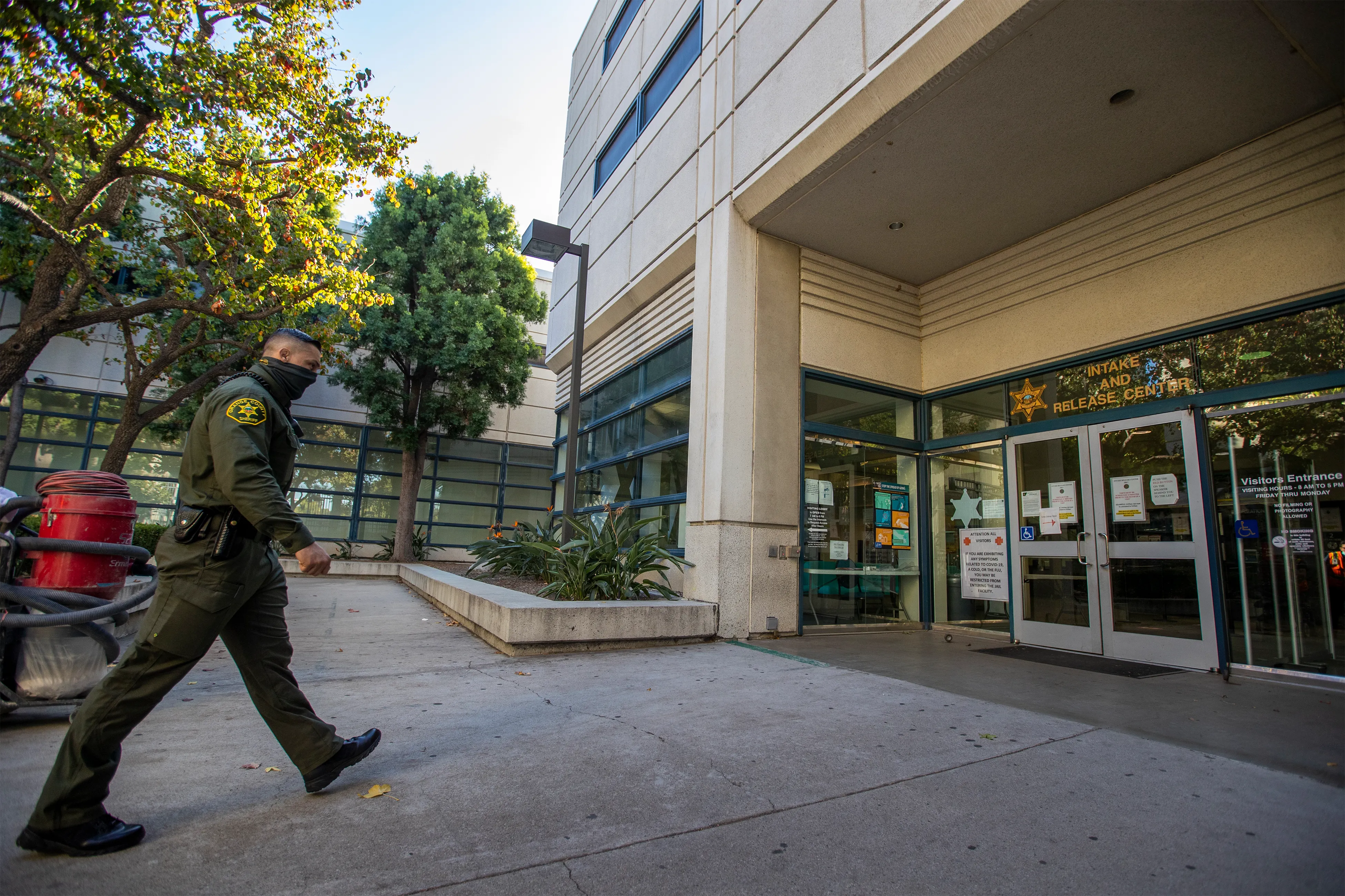 A photograph of a sheriff deputy walking toward the entrance doors of a building that has signage that reads "Intake and Release Center"