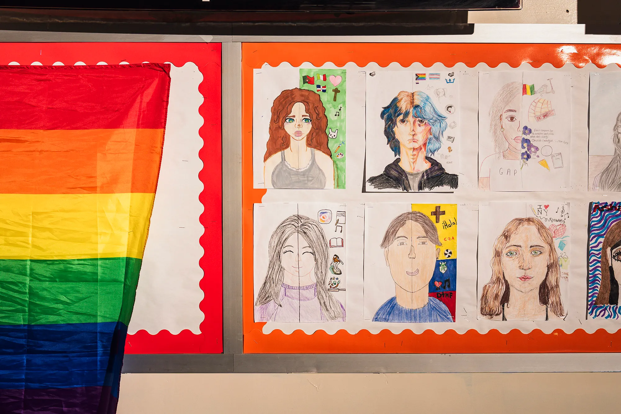 Student self-portraits next to a pride flag in a classroom.