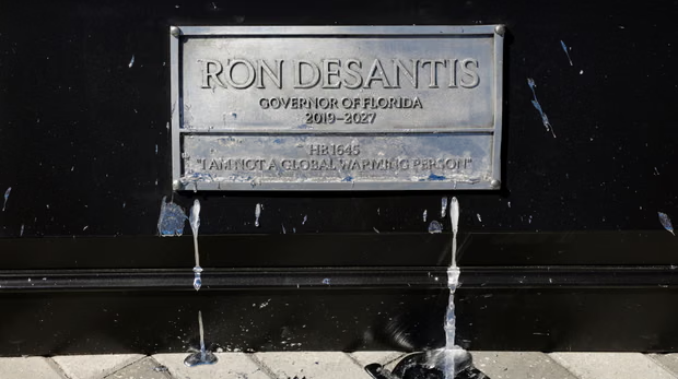 A silver sign that says "Ron DeSantis: Governor of Florida 2019-2027." Below that message says "HB 1645: "I am not a global warming person"